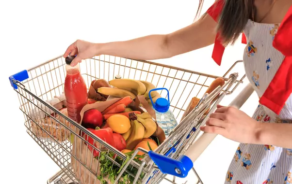 Full shopping cart at store with fresh vegetables and hands close-up.