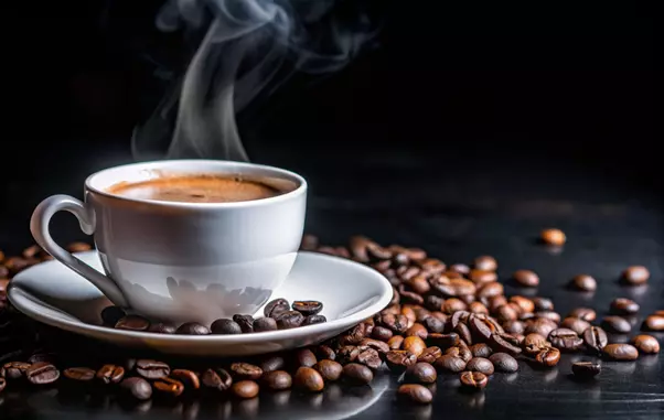 Steaming cup of coffee on a saucer with coffee beans scattered around.