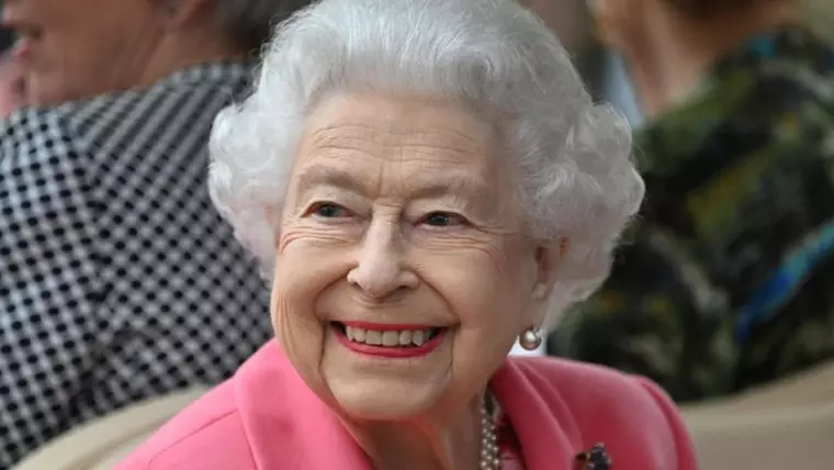 regina elisabeta a II-a, cu parul alb si costum roz, surprinsa in timp ce zambeste. 