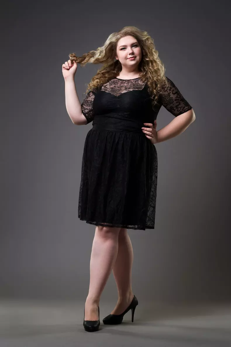 Young beautiful plus size model in black dres, xxl woman on gray studio background