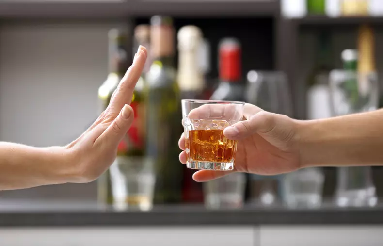 Female,Hand,Rejecting,Glass,With,Alcoholic,Beverage,On,Blurred,Background