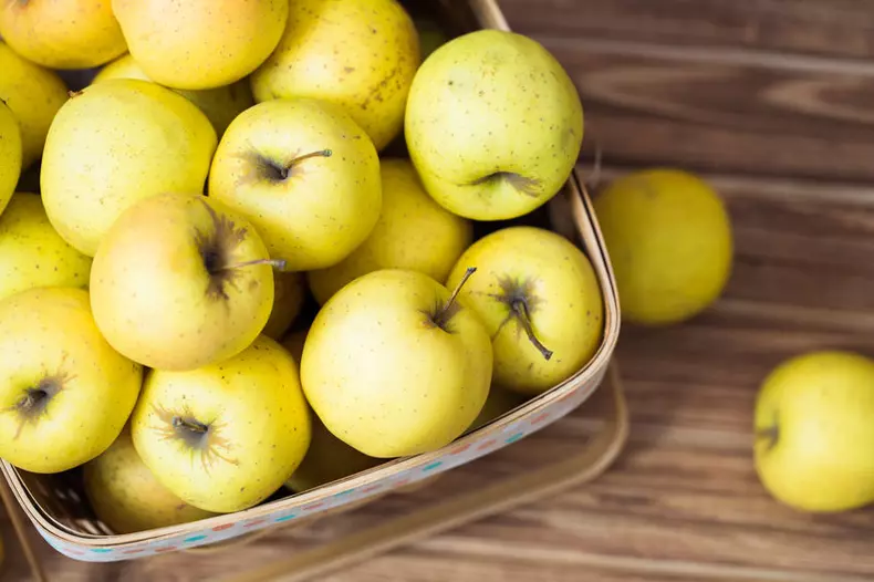 Golden apples in a basket on a wooden background
