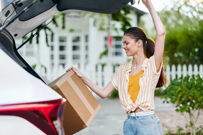 Woman,Unloading,Cardboard,Box,From,Car,,Cheerful,Expression,,Casual,Clothing,