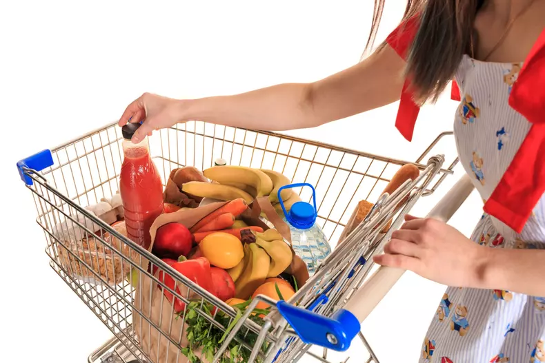 Full shopping cart at store with fresh vegetables and hands close-up.