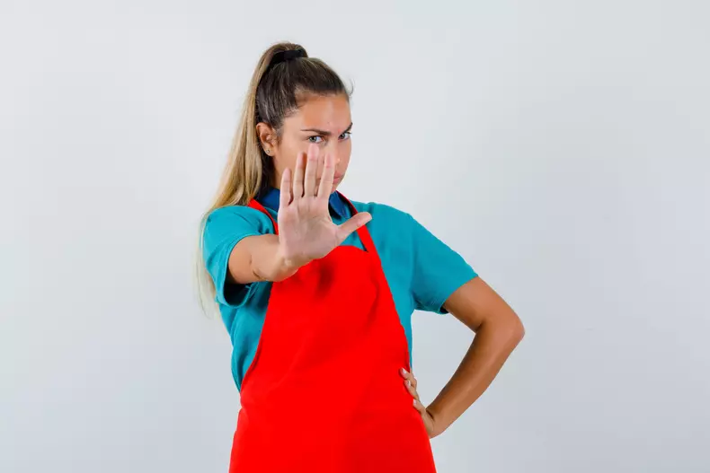 young lady in t-shirt, apron showing stop gesture and looking serious , front view.