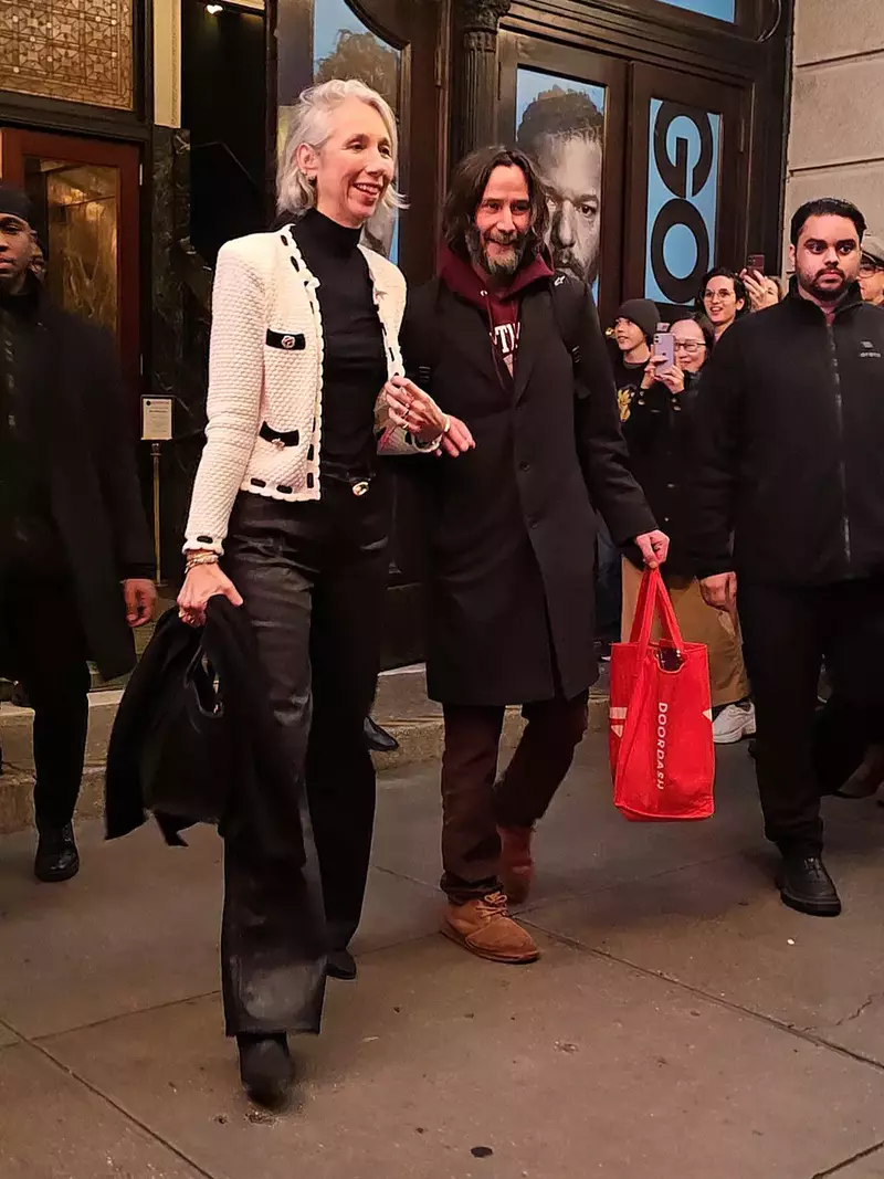 Keanu Reeves holds Alexandra Grant by the hand as they exit his performance of Waiting for Godot and are wished a Happy Thanksgiving by adoring fans outside of the theater in NYC