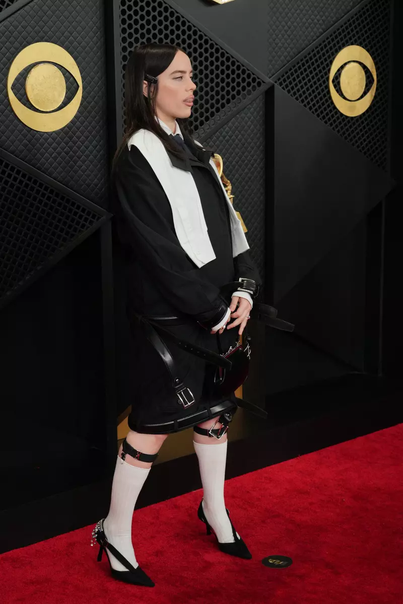 Billie Eilish a ales un stil gotic, inspirat de personajul Wednesday Addams, pentru apariția sa pe covorul roșu la Grammy 2026. Artista a purtat o combinație inedită de jachetă bomber, fustă cu curele și șosete înalte, un look care a divizat criticii de modă.