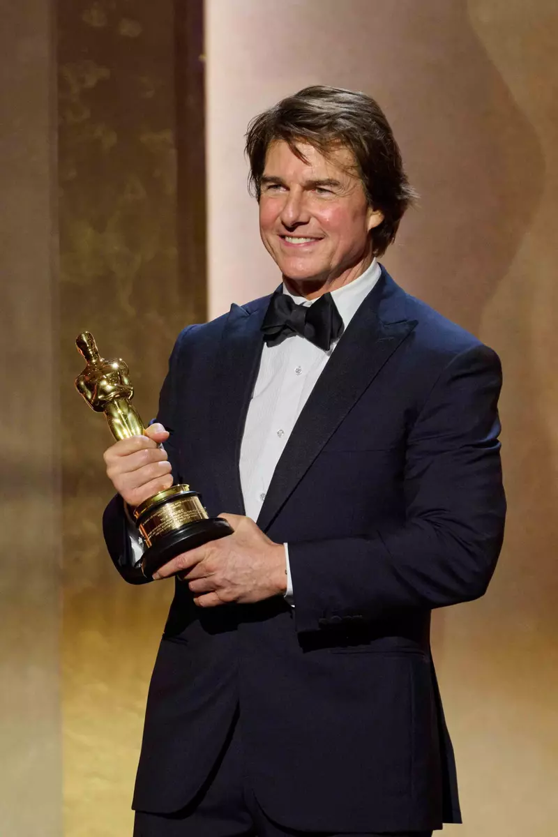 Actorul Tom Cruise zâmbind pe scenă cu trofeul Oscar la Governors Awards 2025, Los Angeles.