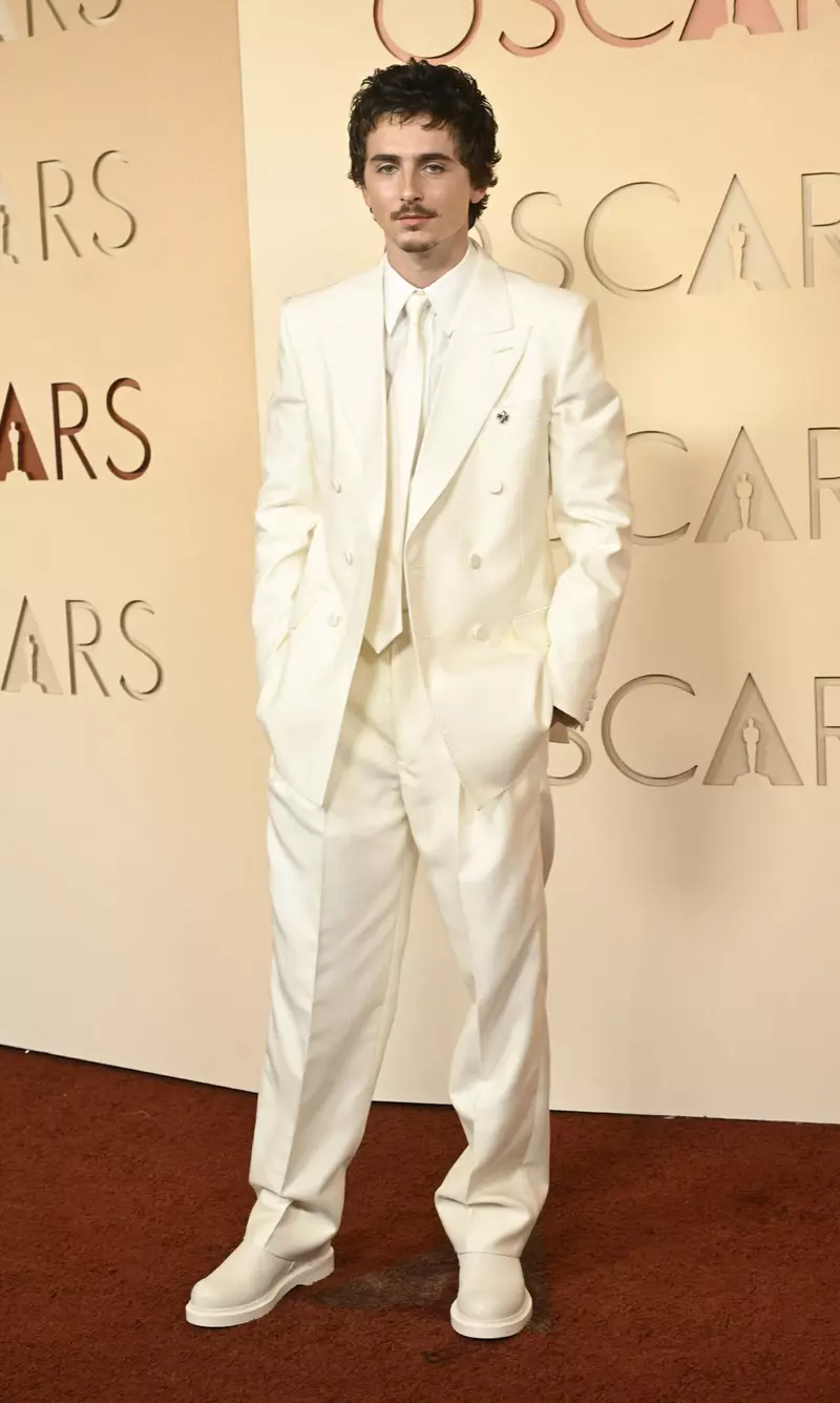 Actorul Timothée Chalamet într-un costum alb Givenchy cu aer retro, purtând ochelari de soare și cizme la Premiile Oscar 2026, Dolby Theatre.